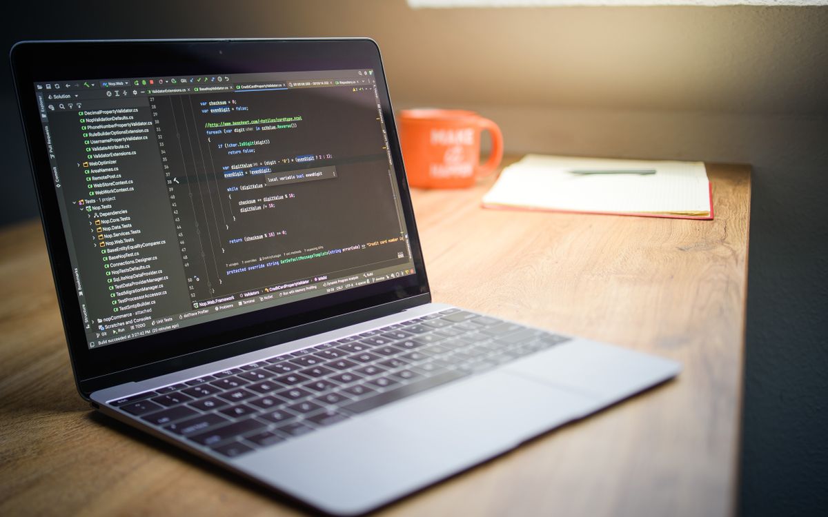 Laptop displaying code beside a notebook and mug