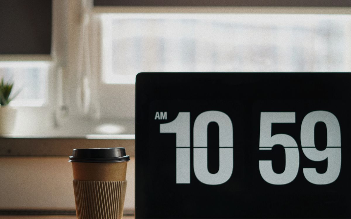 Laptop displaying a clock beside a cup of coffee