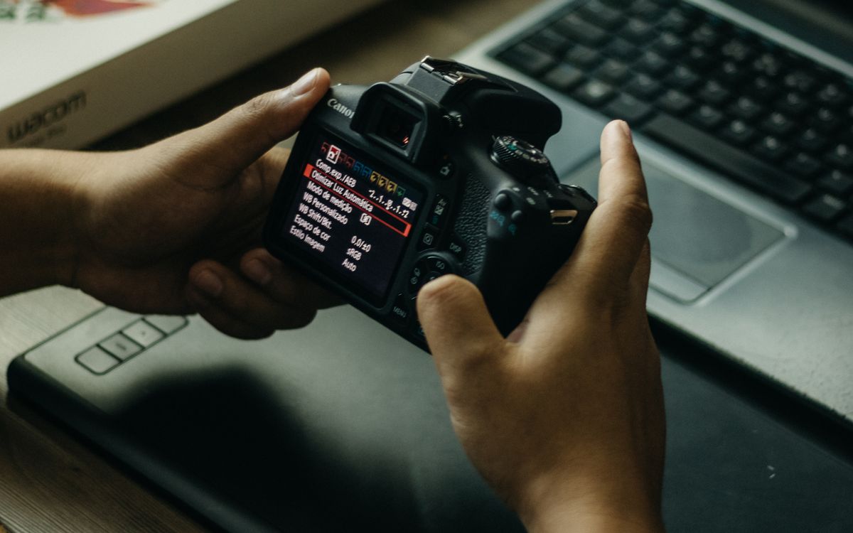 Hands adjusting a camera beside a laptop and graphics tablet